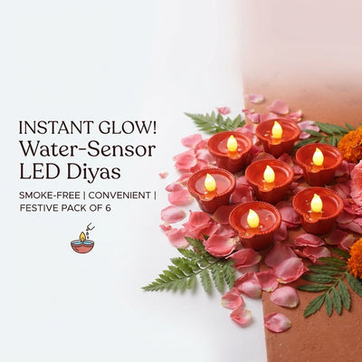 Six water-sensor LED diyas glowing on a terracotta surface decorated with rose petals for a festive setting.